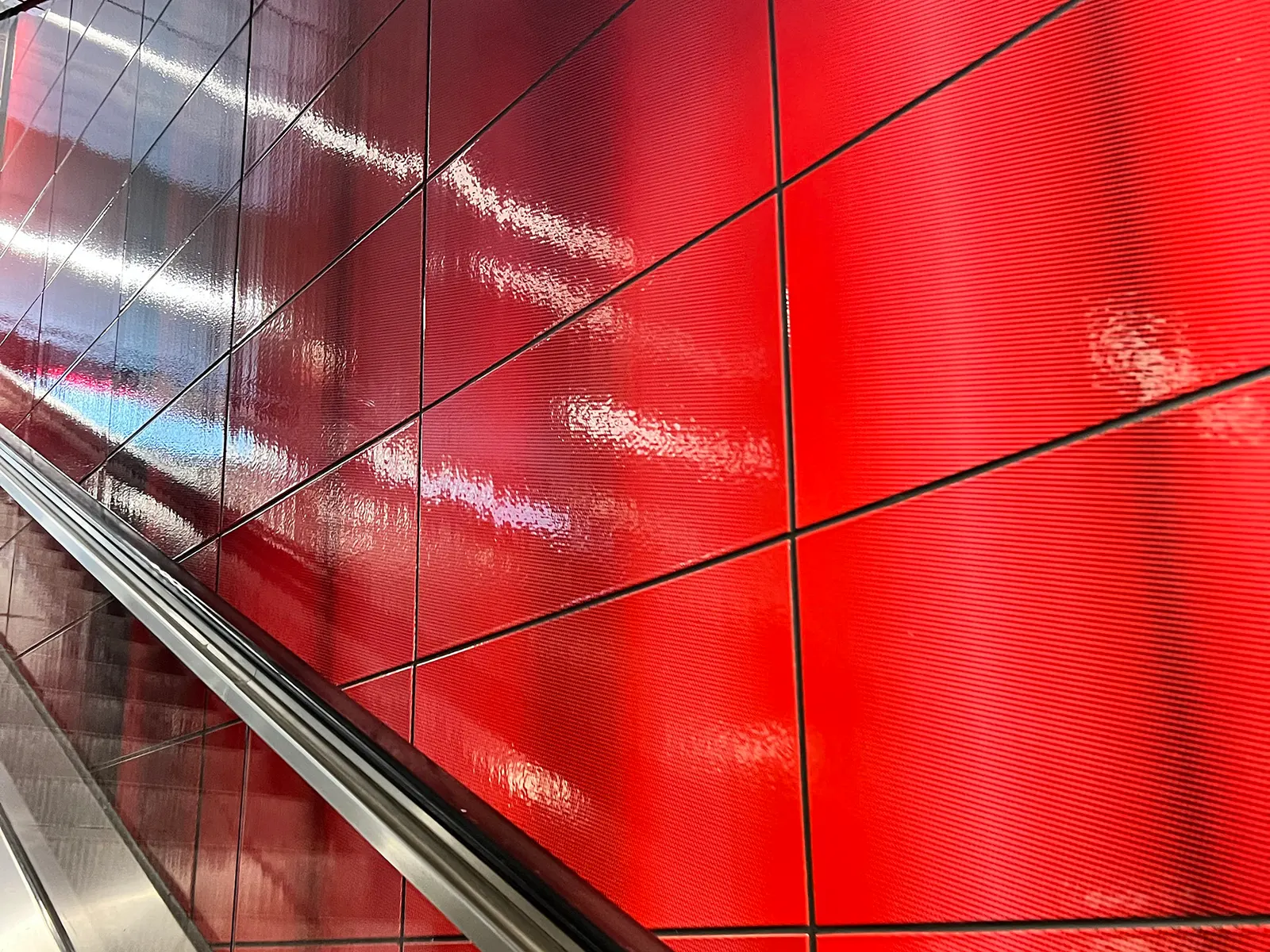 Rote Glasfliesen entlang einer Rolltreppe.